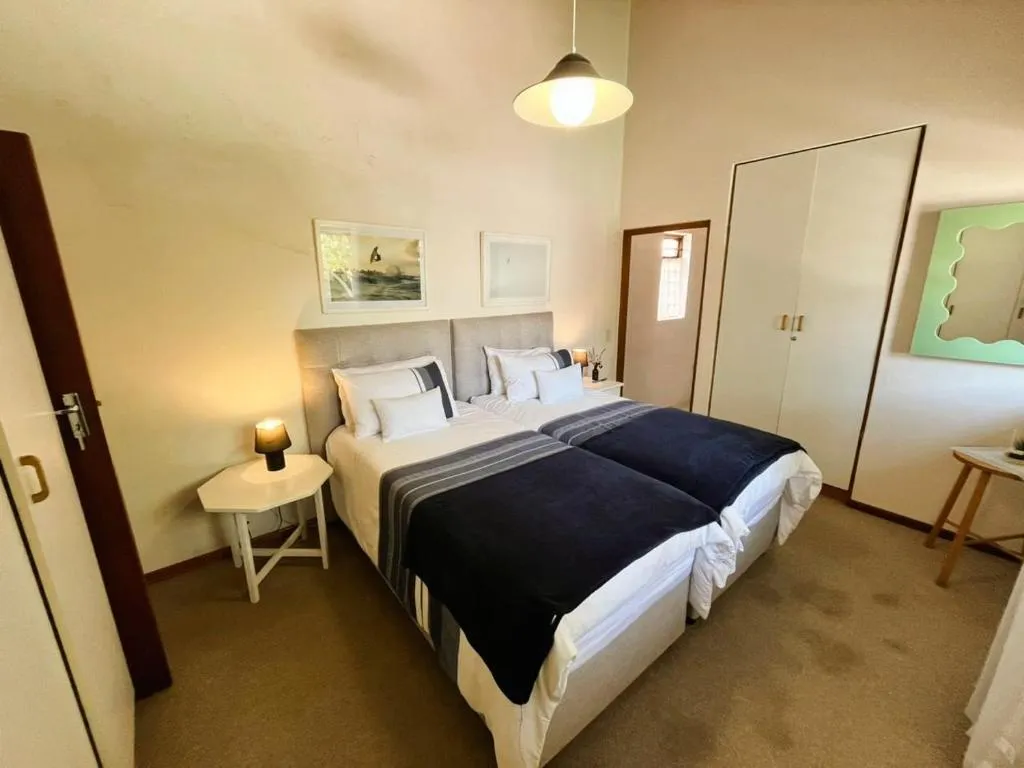 Second bedroom with twin beds pushed together, a white wardrobe and surf-themed artwork