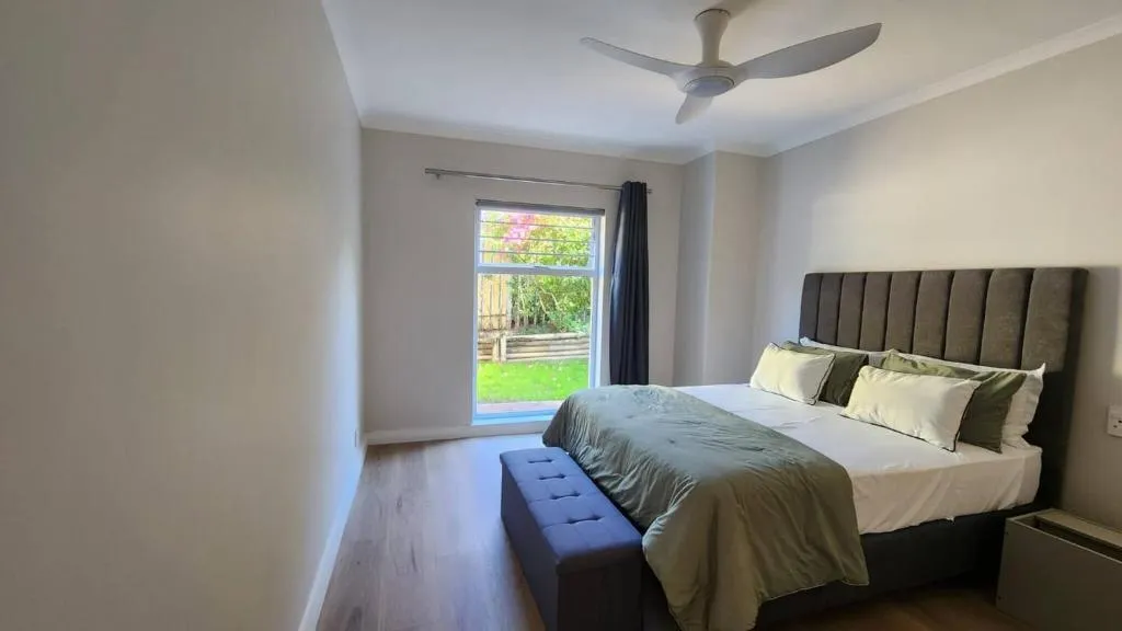 Bedroom with ceiling fan and sliding door onto a small fenced garden