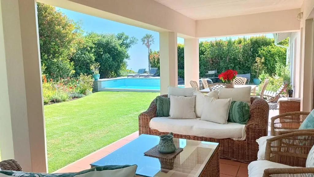 Covered patio lounge overlooking a lawn, pool and lush garden planting