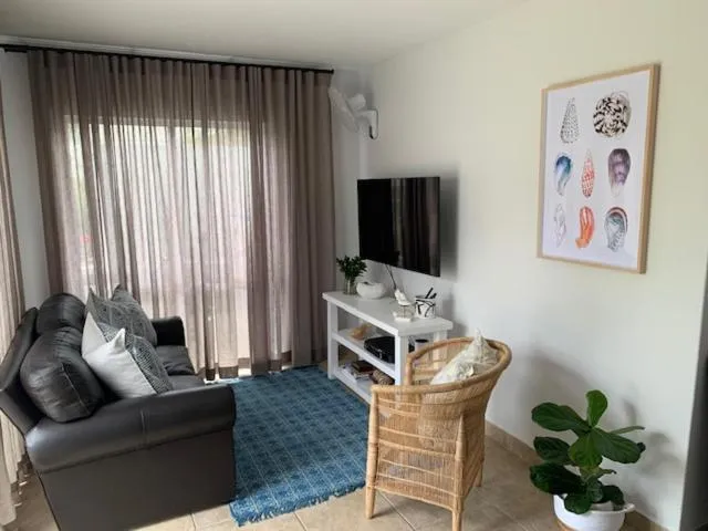 Living room with dark leather sofa, wall-mounted TV, and coastal shell artwork
