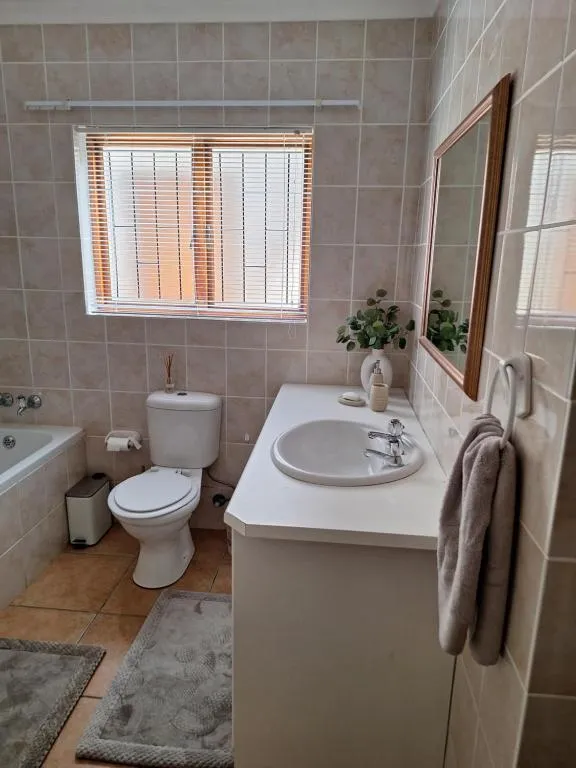 Bathroom with a corner bath, pedestal basin and mirror lit by a curtained window