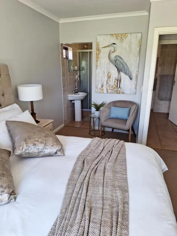 Bedroom with a tufted headboard, wicker armchair and pedestal basin visible through the open en-suite door
