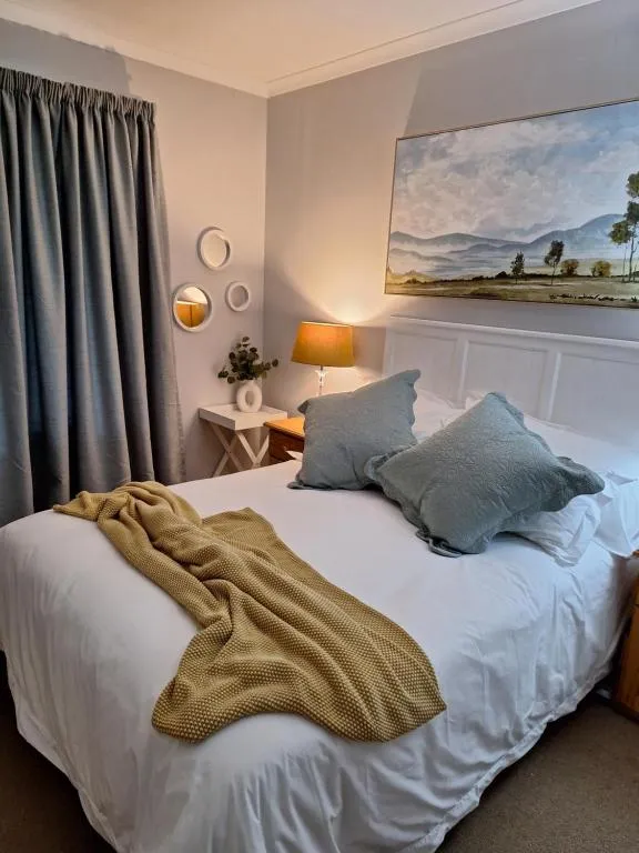 Bedroom in soft grey with a mustard throw, bedside lamp and a framed landscape painting