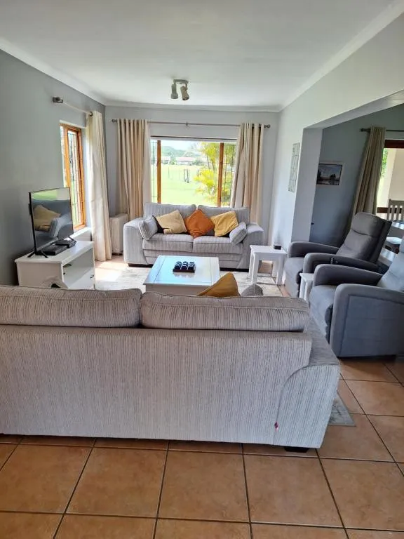 Open-plan lounge with two sofas and armchairs facing a large window over the lawn