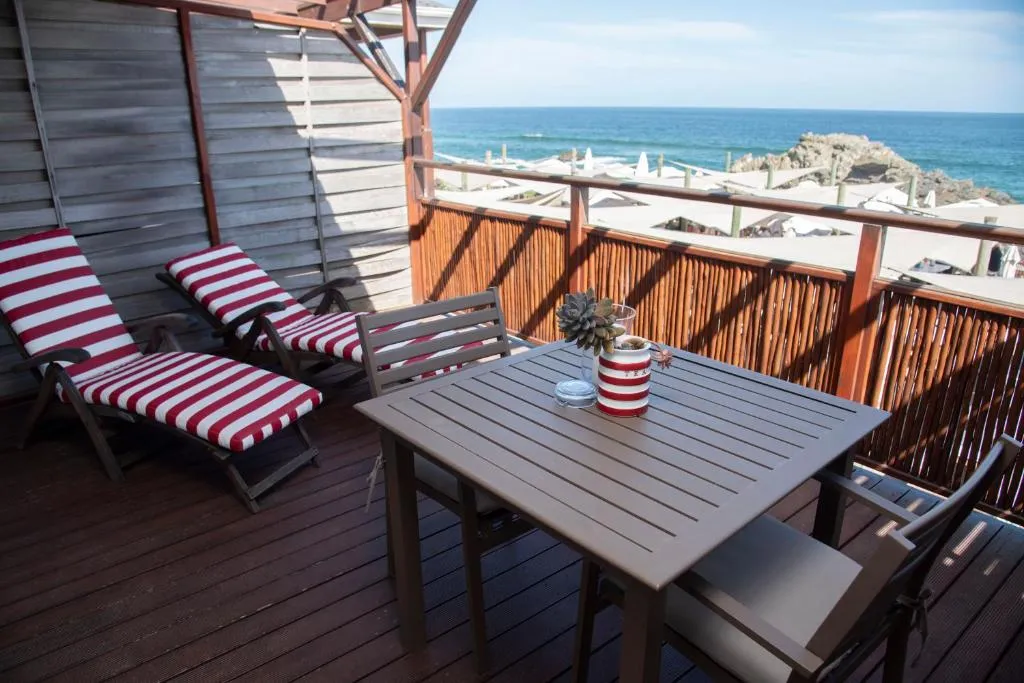 Wooden deck with striped loungers and a dining table looking out over Keurboomstrand beach