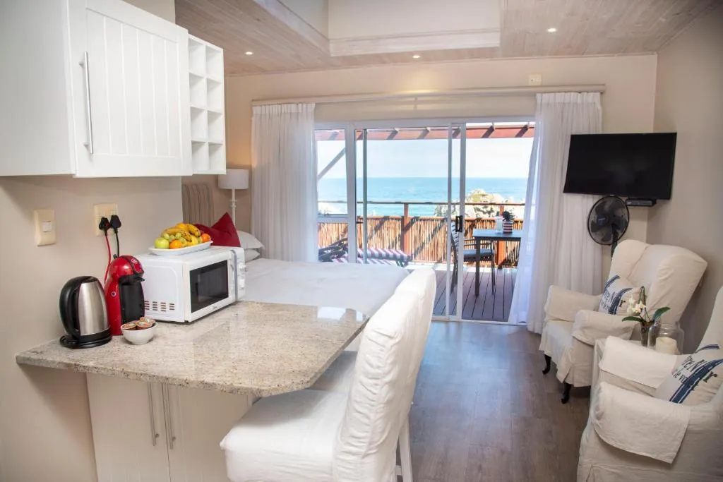 Compact kitchenette with a granite bar counter beside the bed, ocean visible through sliding doors