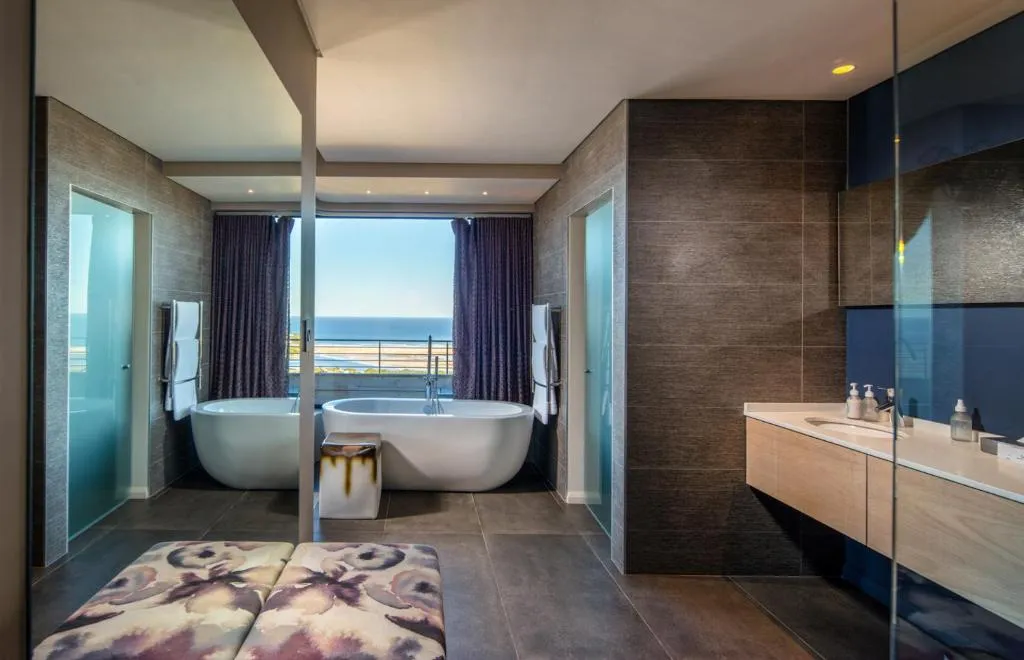 Twin freestanding bathtubs positioned in front of a picture window over the sea
