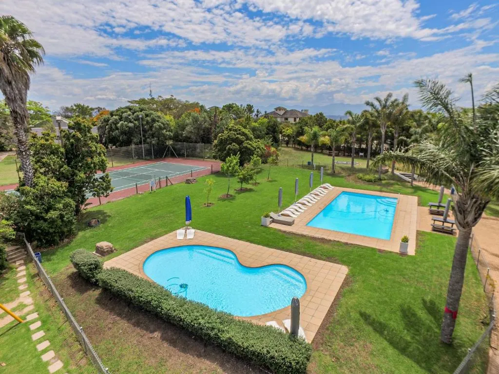 Aerial view of the estate's two swimming pools and tennis court set among palm trees