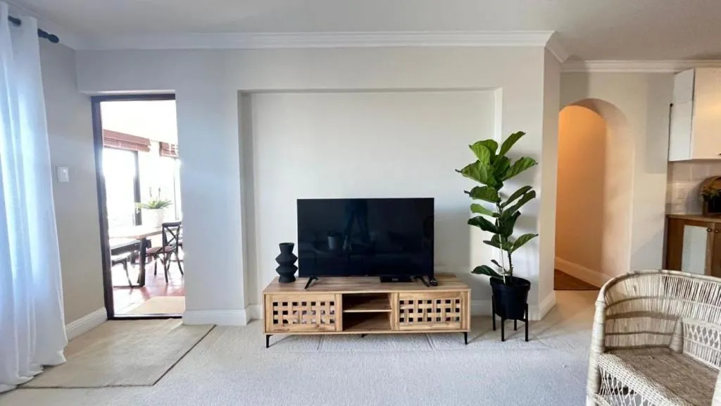 Living room with a wicker armchair, wall-mounted TV, and an archway through to the kitchen