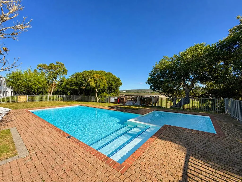 Shared swimming pool on a paved terrace with lawn and lagoon views beyond