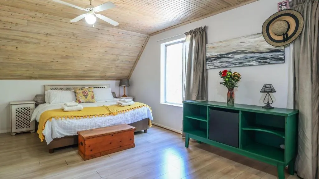 Attic bedroom with a sloped timber ceiling, ceiling fan, and a mustard throw folded on a queen bed