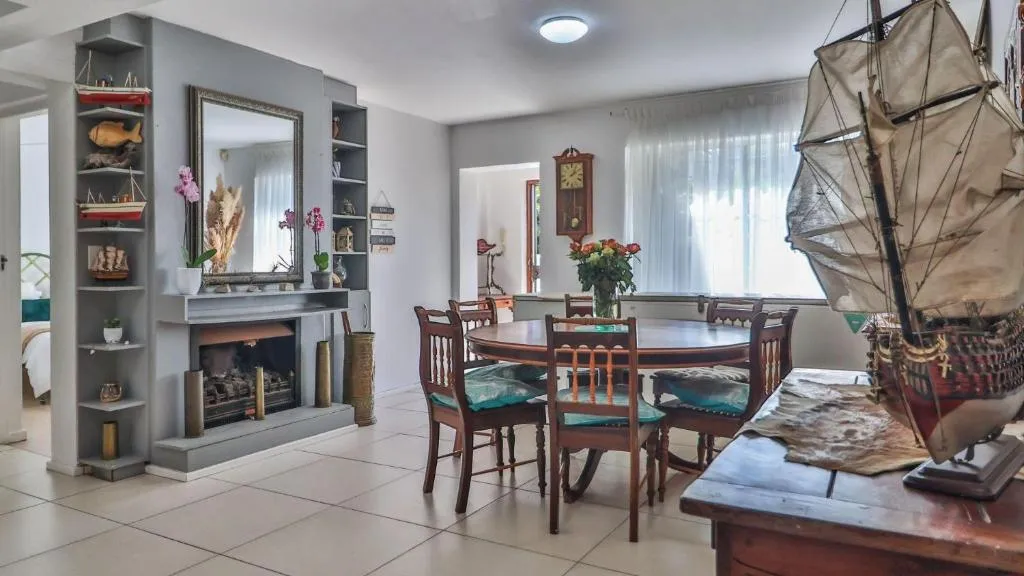 Round dining table for six beside a tiled fireplace mantel styled with model ships and nautical curios