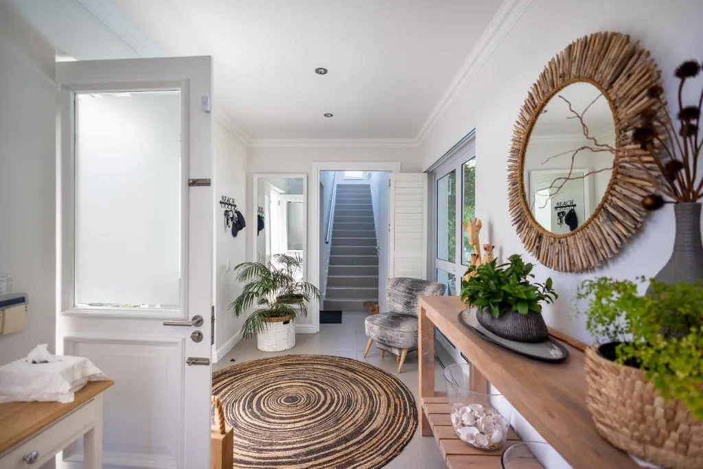 Entrance hallway with a driftwood-framed mirror, a round woven rug and a staircase beyond