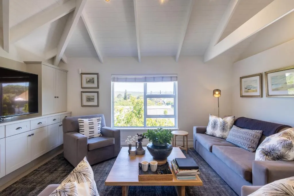 Living room with a vaulted beamed ceiling, grey sofas and a window over the treetops and hills