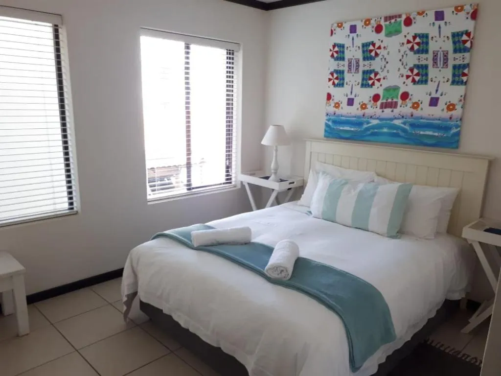 Bedroom with a double bed dressed in white linen, teal accents and a colourful beach-themed canvas