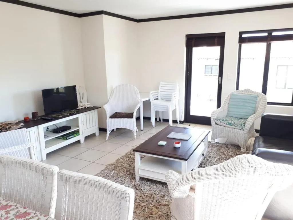 Living room with wicker armchairs, a black leather sofa, wall-mounted TV and doors onto a balcony