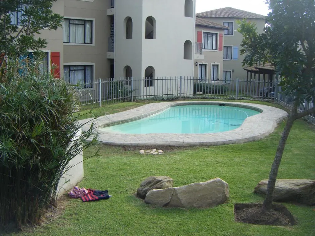 Shared kidney-shaped pool on the Santini Village estate lawn, fenced and surrounded by apartment blocks