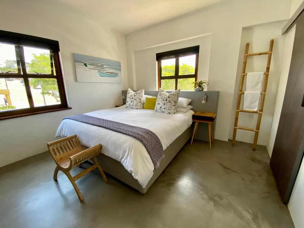 Bedroom with a boat-themed painting, bamboo towel ladder, and windows onto the street