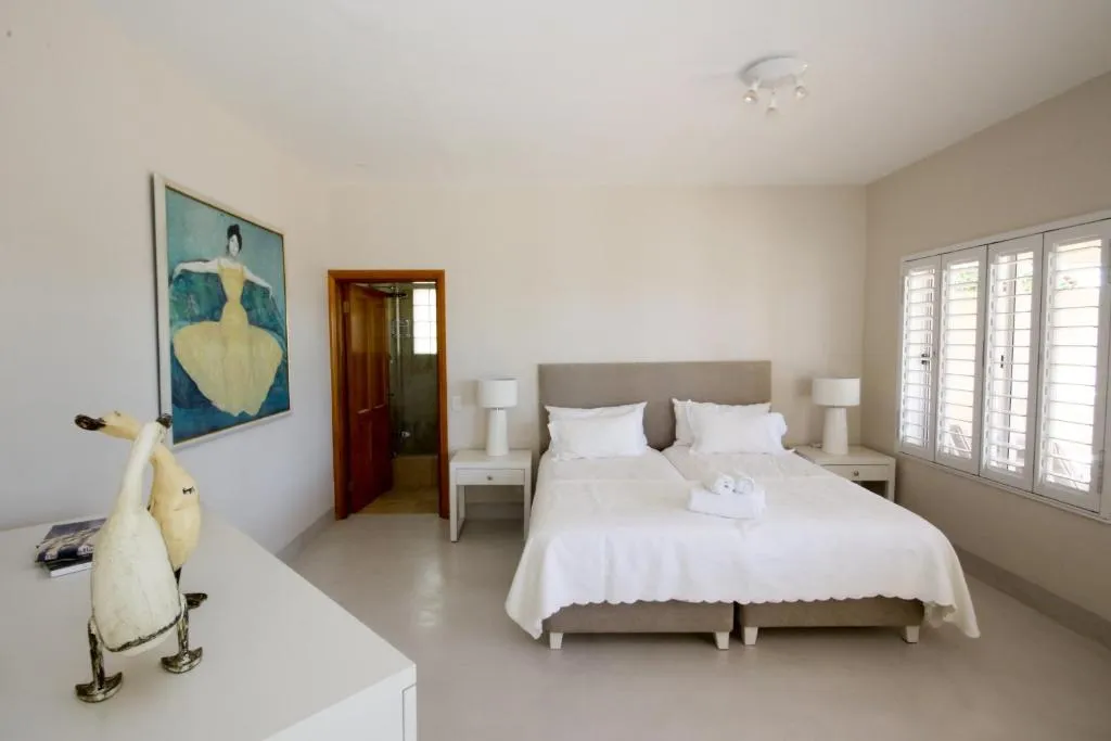 Twin bed guest room with a framed art print, bedside lamps and louvre shutters