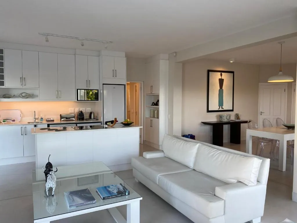 White fitted kitchen open to a dining table and lounge with a sculptural pendant light