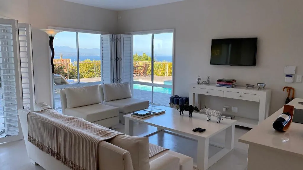Lounge with white sofas opening through shuttered doors to a pool deck and sea view