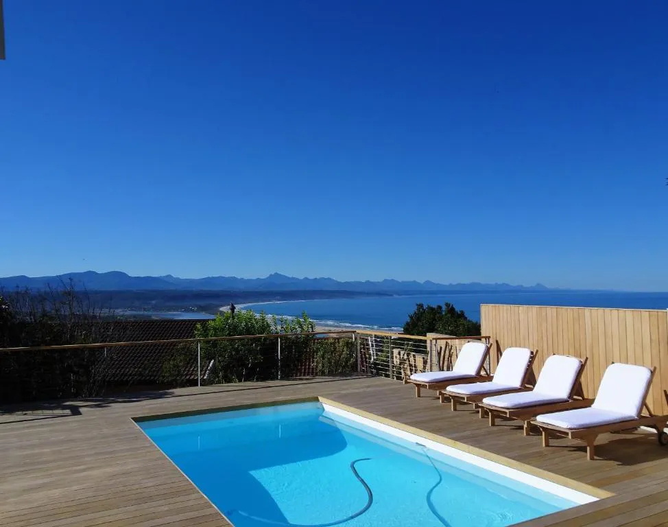 Rooftop pool deck with a row of loungers overlooking Plettenberg Bay beach and mountain coastline
