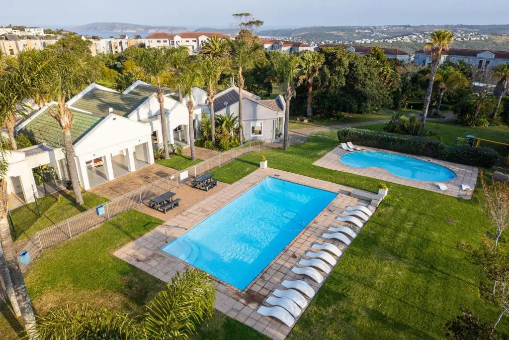 Aerial view of the estate's two swimming pools, lawns and loungers with the coastline beyond