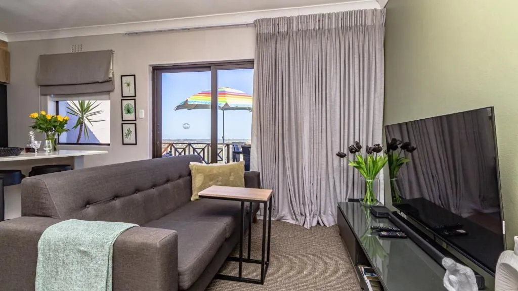 Living area with a grey sofa, wall-mounted TV and sliding doors onto a balcony with a sea glimpse
