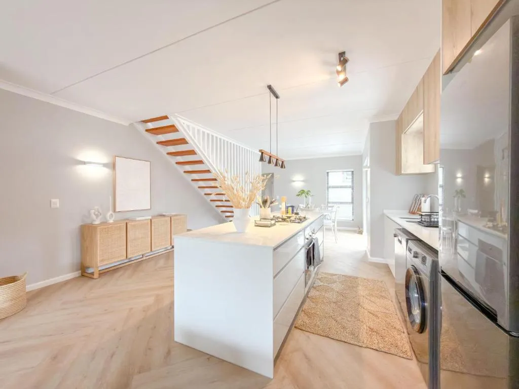 White kitchen island with pendant lights, a gas hob and an open-tread staircase behind