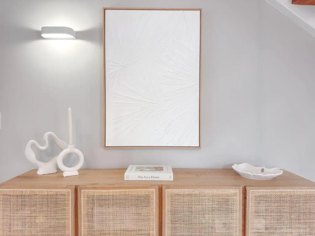 Close-up of a rattan sideboard with a ceramic candle holder and textured artwork