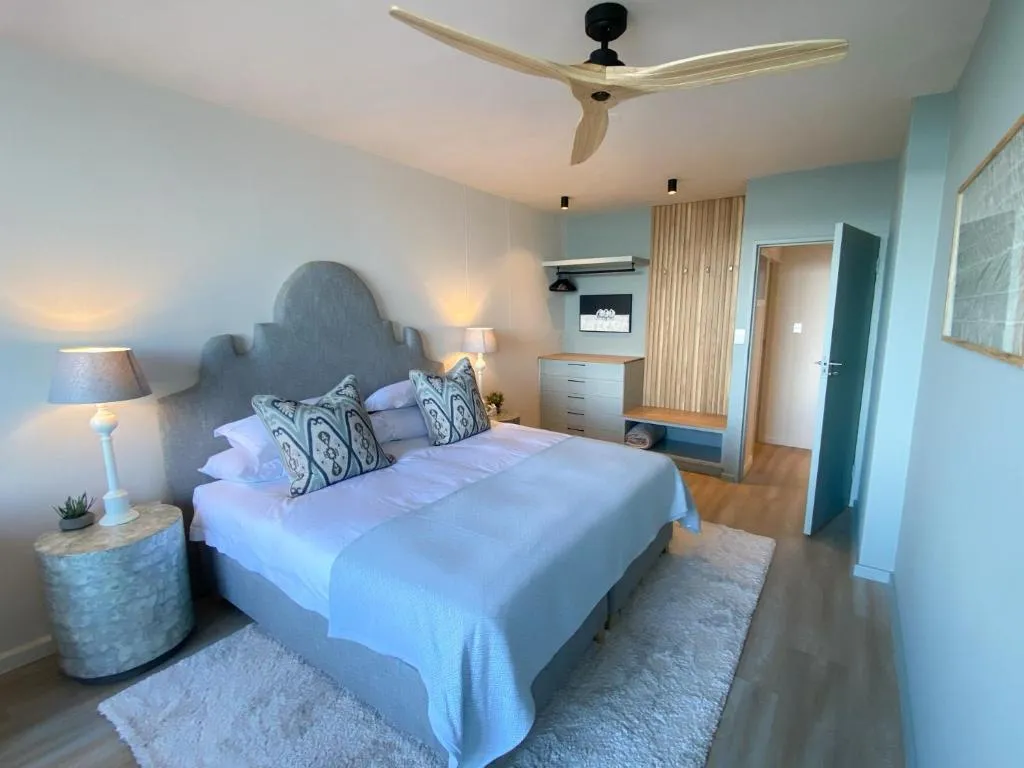 Bedroom with a grey upholstered headboard, wooden ceiling fan and soft rugs