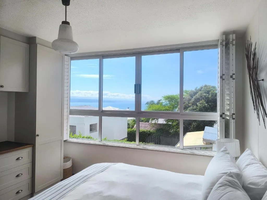 Bedroom with a wide sliding window framing an open sea view over neighbouring rooftops