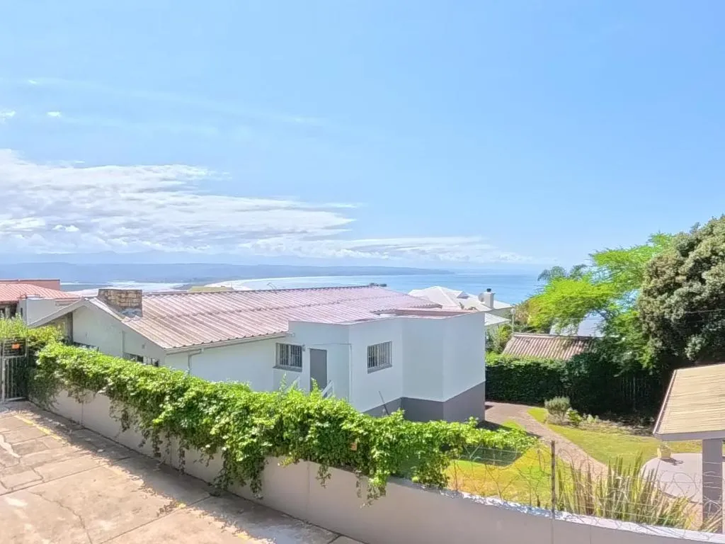 Whitewashed house behind a hedge with Robberg Beach and Plettenberg Bay visible beyond the neighbourhood
