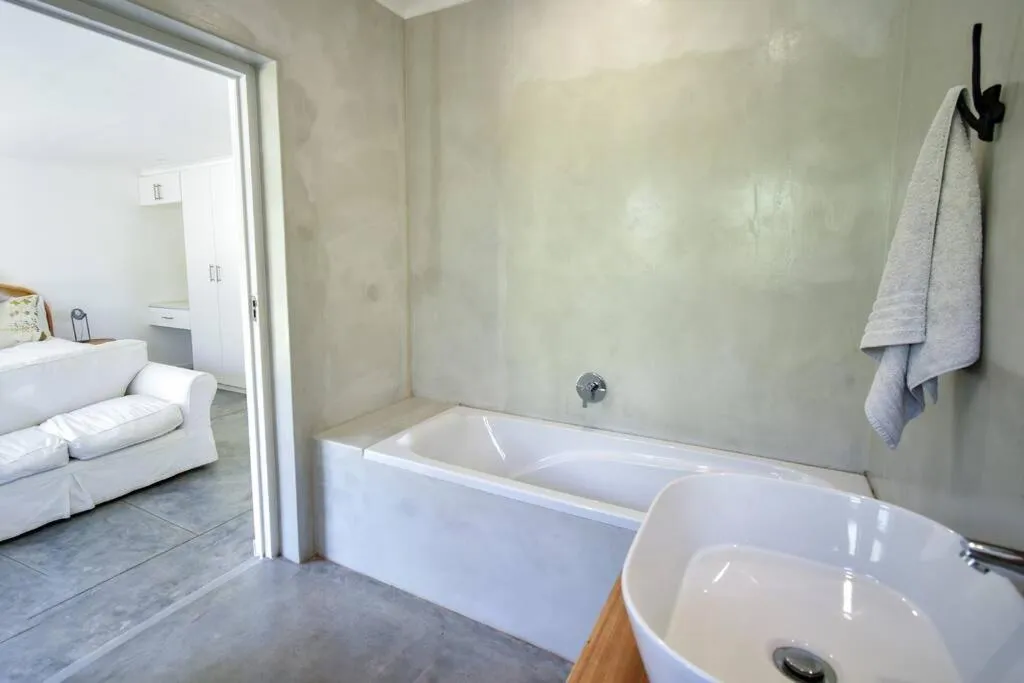 Bathroom with a built-in bathtub and smooth-plaster walls, door open to the lounge beyond