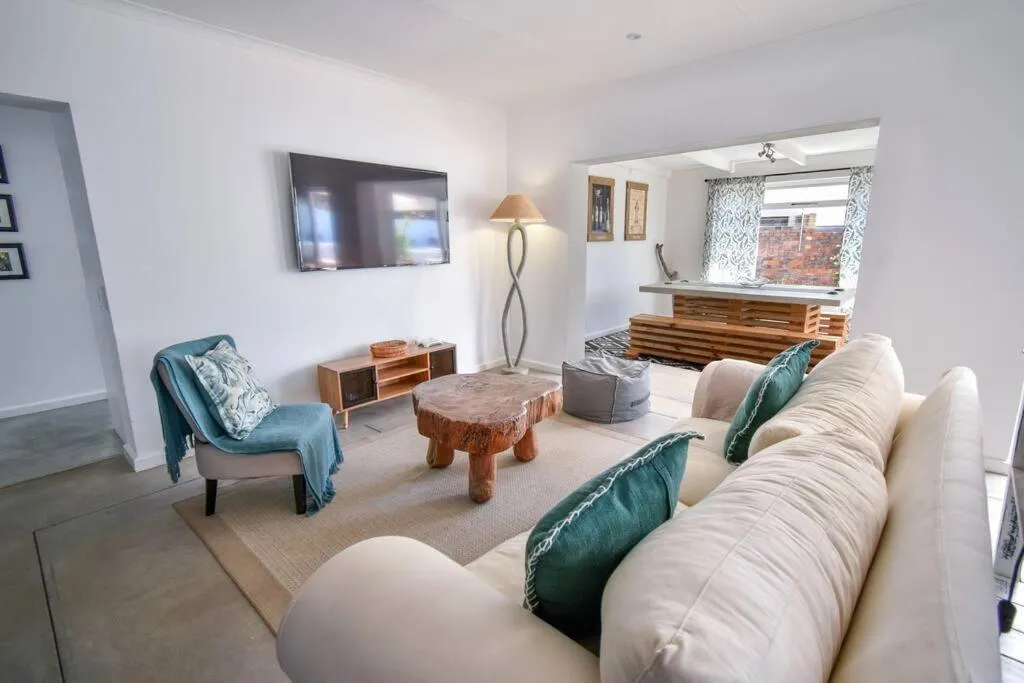Second living space with a wall-mounted TV, teal armchair and sofa opening to a dining nook