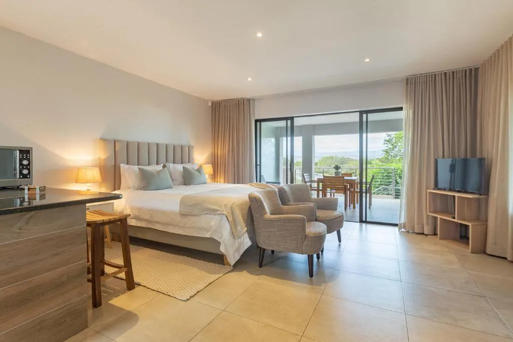 Bedroom with reading chairs beside sliding doors onto a balcony overlooking the hills