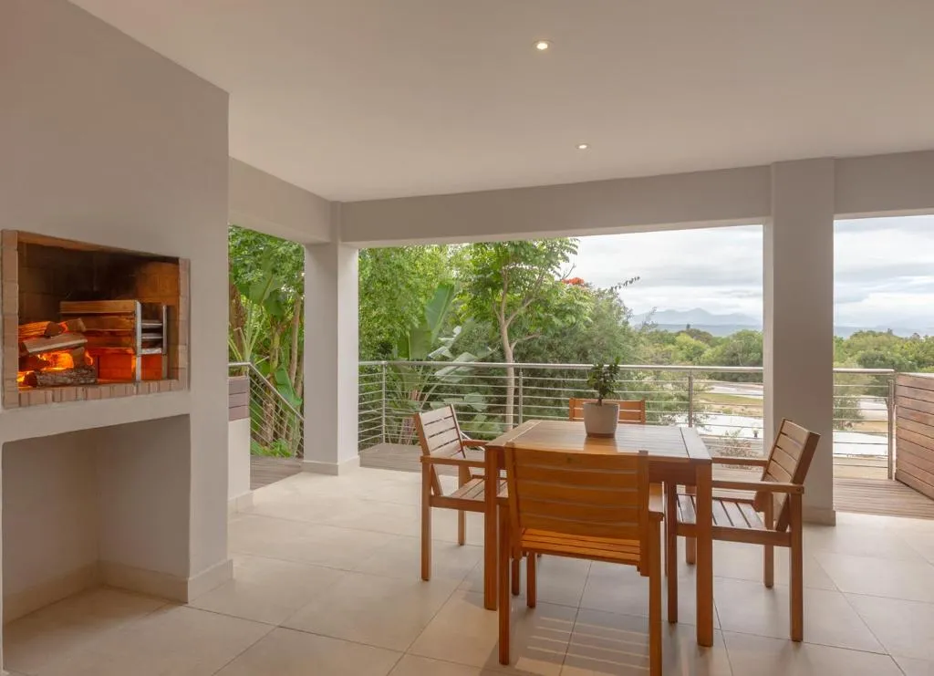 Covered terrace with a built-in brick braai and wooden dining table looking over treetops