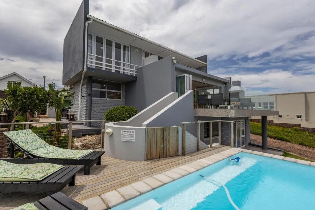Two-storey house exterior with sun loungers on a wooden deck beside the swimming pool