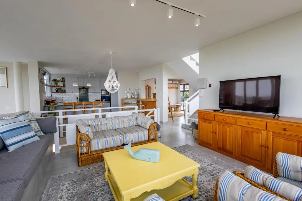 Open-plan lounge with striped rattan sofas, a yellow coffee table, and the kitchen beyond
