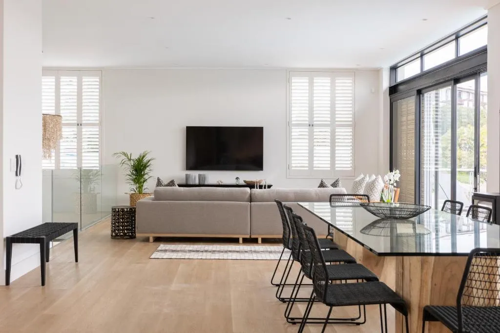 Living area with sectional sofa, wall-mounted TV and glass-top dining table opening onto a balcony