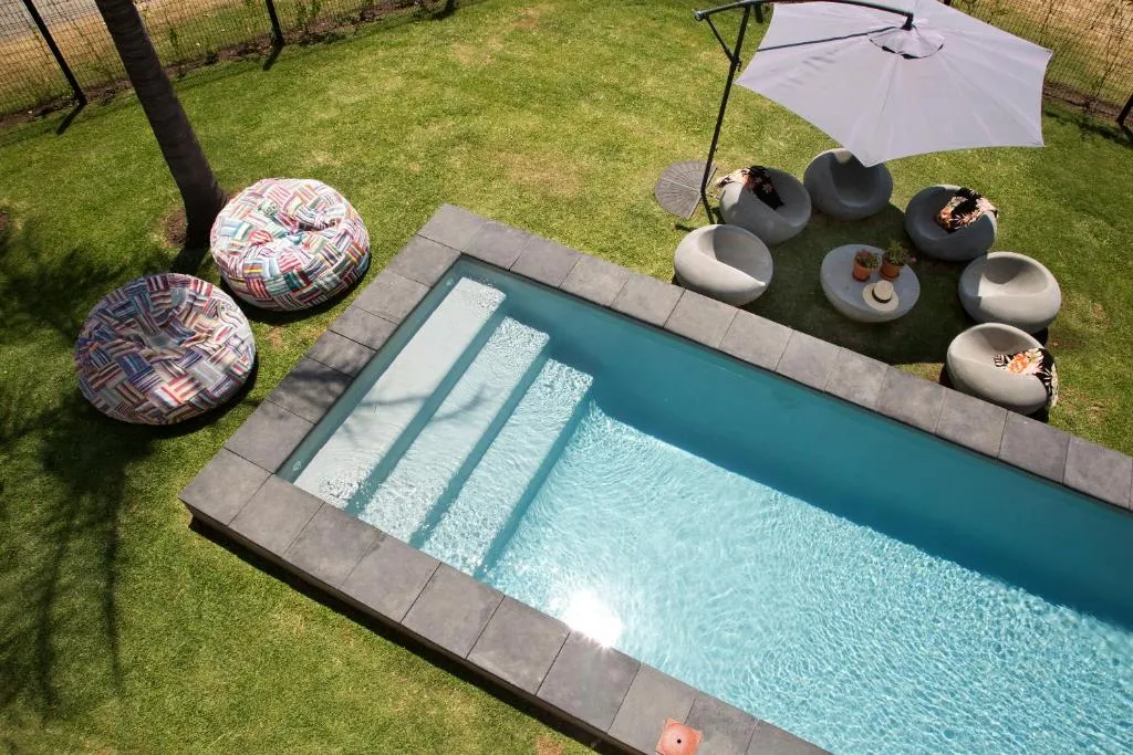 Aerial view of the stepped pool with woven pouf seating and a shade umbrella on the lawn