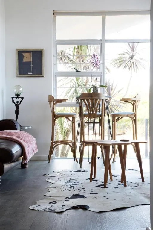 Dining nook with rattan bar chairs, a cowhide rug and palm views through floor-to-ceiling windows