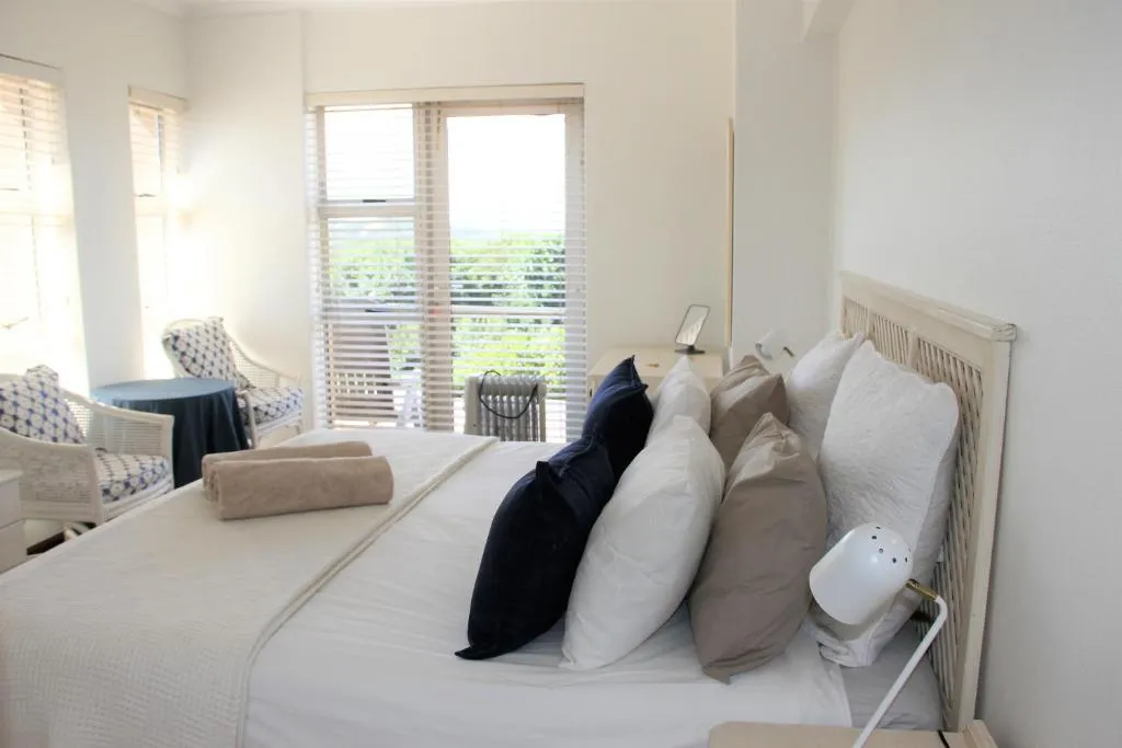 Bedroom with a wicker headboard, sitting nook and sliding door onto a leafy garden view