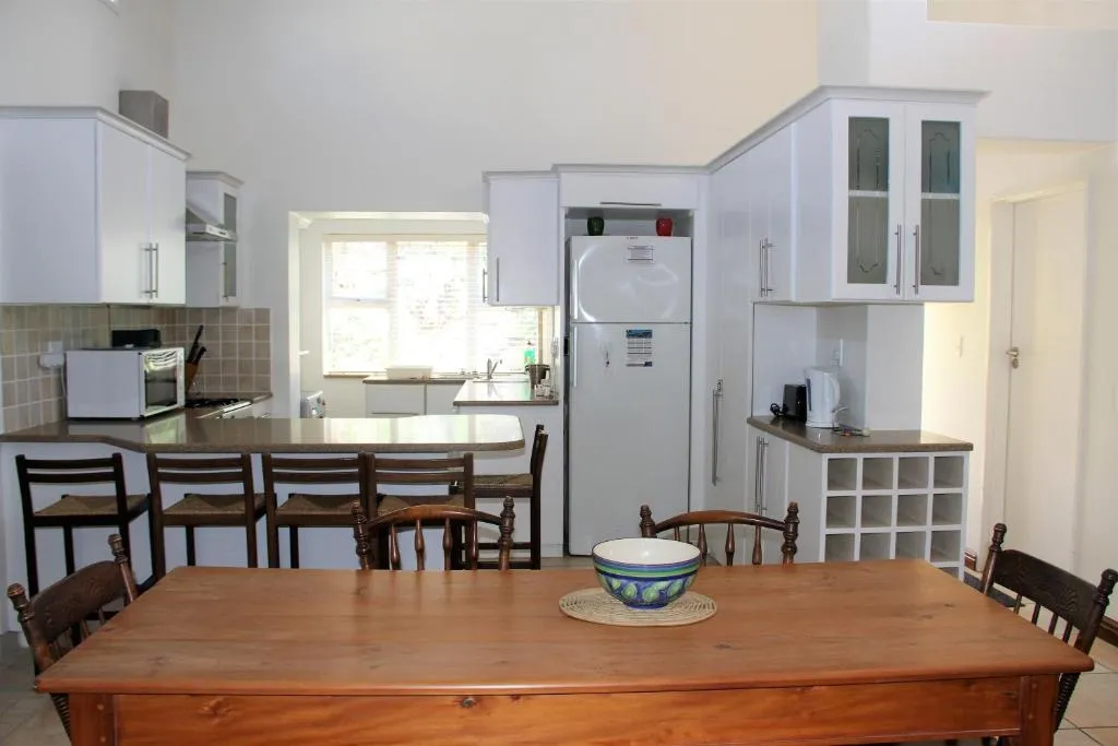 Farmhouse-style dining table in front of the fitted kitchen with fridge and wine rack