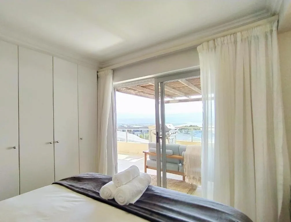 Bedroom with sliding doors open to a terrace, ocean visible past the pergola beyond
