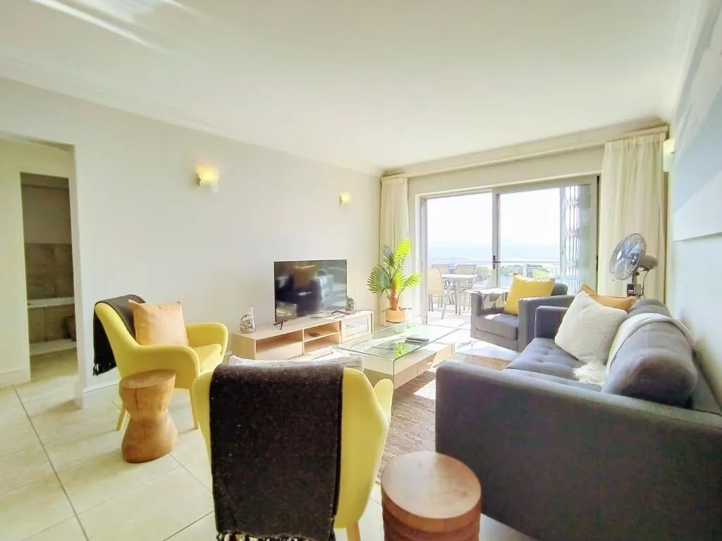 Living room with yellow accent chairs, a grey sofa and a sliding door onto the terrace with sea views