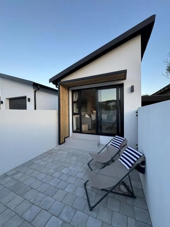Angular modern pod exterior with a private paved courtyard and two deck chairs at dusk