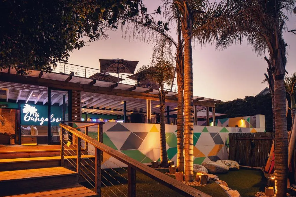 The Bungalow's illuminated deck and tiered rooftop terrace at dusk among palm trees