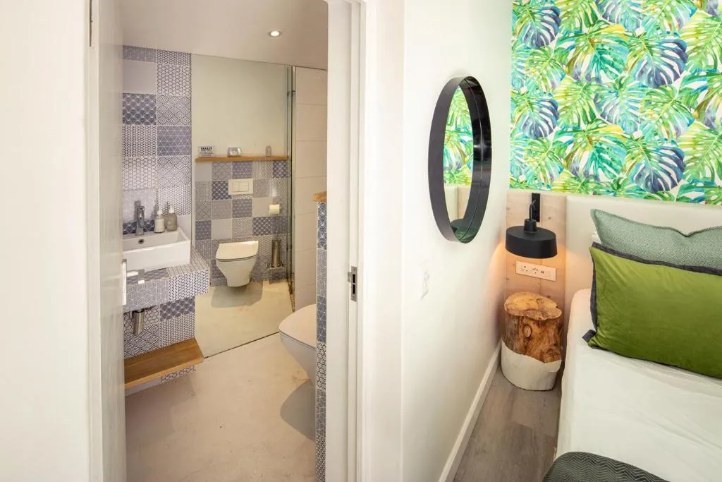 En-suite bathroom with patterned blue tiles beside a bed with tropical leaf-print wallpaper