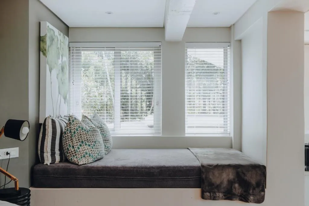 Window seat nook with patterned cushions looking out through wooden blinds to the garden